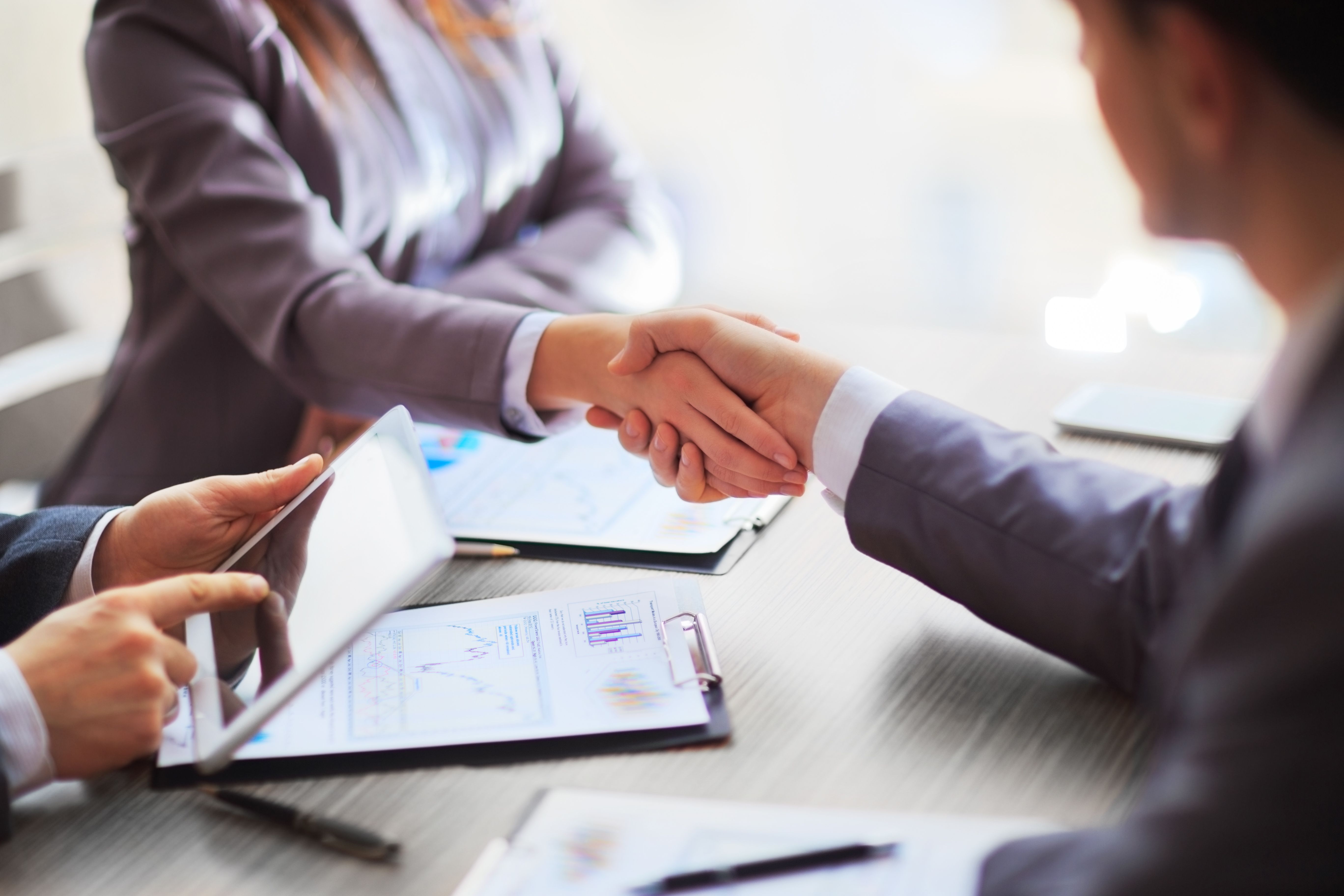 Two people shaking hands over a conference table